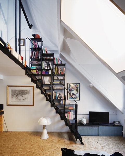 A black steel staircase with integrated storage leads up to a lofted bedroom