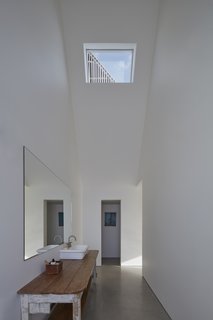 The sink in the bathroom is created out of an old wooden table and a new sink basin, providing texture and patina in the otherwise pristinely white space.