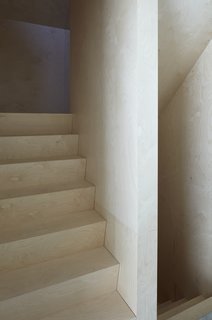 Wood plays a dominant role on the upper floors and the staircase leading up to it. The walls and floors are clad in birch plywood, and the detailing is precise and minimalist.