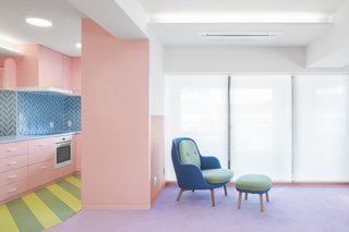 The rosy, dull pink of the kitchen cabinets bleeds into the living room but is starkly contrasted with the striped green-and-yellow floor and blue backsplash in the kitchen and furniture in the living room.