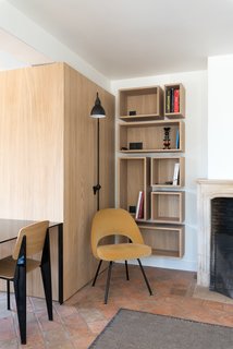 Old meets new at this corner of the living and dining area, where an original mantle with a decorative profile sits comfortably next to open wood shelving with minimalist detailing and a soft yellow chair.