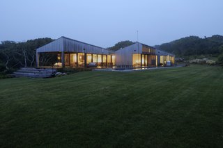 While the view from the driveway presents the home as mostly solid with a central glazed void connecting the two volumes, when approached from the beach, the home appears much more open, with an outdoor covered porch and glazed walls.