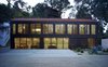 A new two-story building, consisting of a garage on its first level and a private library on the second level, includes storage, a reading area and a powder room. The illuminated facade is made of bronze-anodized aluminum metal panels. Photo of Morgan Phoa Library and Residence modern home