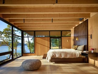 The upper level of Pole Pass Retreat by Olson Kundig consists of a single bedroom that cantilevers out beyond the enclosed volume below to create a covered, outdoor storage space at the rear of the house. The second story looks out over the drought-resistant, planted roof of the main level, giving the sense of floating above the lawn and water beyond. 