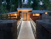 Modern home with Exterior, House Building Type, Stone Siding Material, Wood Siding Material, and Metal Roof Material. Bridge Entry | To enter the home, guests arrive on an upper bluff and cross a foot bridge to the front door. The bridge draws immediate attention to the home’s signature folded roof plane, which appears to hang effortlessly in the shadow of a deep canopy of cottonwood trees. Photo 3 of Woody Creek Residence
