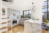 The kitchen’s standout feature is the Carrara marble backsplash and 2-inch-thick countertops with a waterfall edge. Ikea cabinets with blue-gray fronts offset the white marble and are adorned with simple hardware in a satin nickel finish. On the peninsula side of the kitchen’s U-shaped counters, refrigerator and freezer drawers are tucked discreetly underneath to reduce visual clutter and maximize space efficiency. A stainless steel undermount sink is matched to an industrial faucet and sprayer.
On the side of the peninsula that faces the living room, the ledge of the counter was extended to create a space for bar seating with built-in 12-bottle wine storage as well. Photo 2 of A Greenwich Village Loft Gets a Makeover modern home