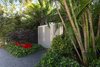 Modern home with Outdoor, Front Yard, Garden, Hardscapes, Gardens, Trees, Walkways, Raised Planters, Shrubs, Pavers Patio, Porch, Deck, Landscape Lighting, and Metal Fences, Wall. A dynamic entrance to the garden framed by mass plantings and bright sculptural containers sets the scene for the tropical garden behind the closed doors. Photo of Von Phister