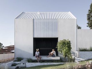 Soft gray concrete, a polycarbonate screen, and metal roof bedeck the simple front facade of House A. Not immediately apparent? An underground water collection tank and solar panels. "We used a really high recycled content mix for our tilt-up concrete walls, which have 65-percent slag [a byproduct of steel production] instead of high-carbon emitting Portland cement," say the architects.