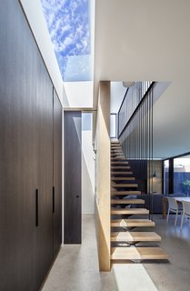 A staircase with floating oak stair treads and a continuous steel railing goes up to the second floor. The cupboards on the left are fronted with the same "Ravenswood" panels, and a skylight floods the space with light.