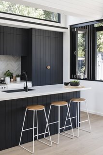 The dark kitchen cabinetry is a nod to the exterior, "as the pattern of the shiplapped cladding informed the grooves of the kitchen joinery," says the firm.