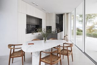 In the kitchen, Hans Wegner chairs surround a vintage triangular marble dining table from Willy Ballez. The island pendants are by Davide Groppi, and the kitchen system is Rossana, an Italian luxury kitchen brand.