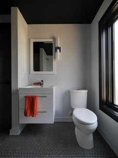 In the bathroom, a wall-mounted vanity saves floor space, and charcoal penny tiles sync with the dark-hued trim found throughout the house.