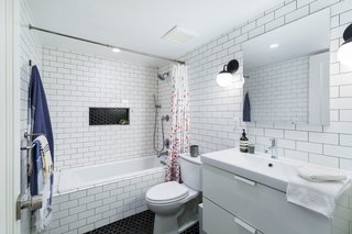 A classic scheme in the apartment bathroom utilizes white subway tile and two-inch black hex tile, both from Nemo. The vanity was sourced from IKEA, and a Cedar & Moss sconces flank the mirror.