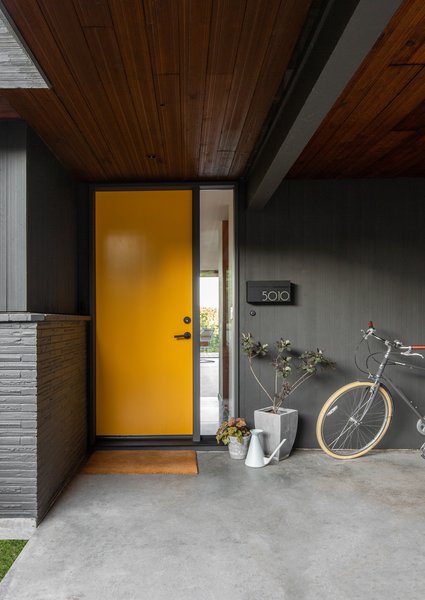 A combed cedar plank soffit sits above the refreshed front door. The opaque glass was replaced with clear glass so the owners can see out, and the wall-mounted mailbox is from V Sons Designs.