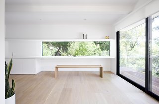 An integrated desk and wall shelf, the latter incorporating hidden LED lighting, frame a ribbon window that appears frameless to better merge with the treetop view. 