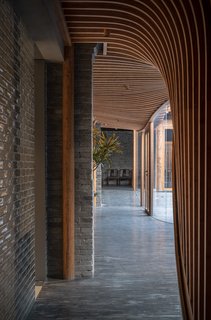Curvilinear wood slats form the interior ceiling of the inserted veranda. A tile wall mimics the original restored brick.