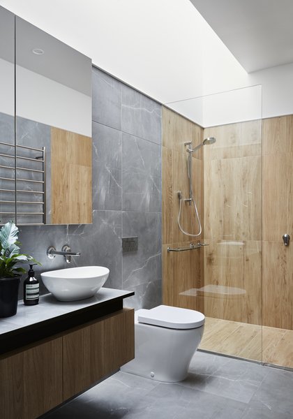 The floor, walls, and vanity in the master bathroom all sport the same porcelain tile for visual consistency, while textured porcelain tiles that look like wood distinguish the shower. A new skylight sheds light inside the internal room.