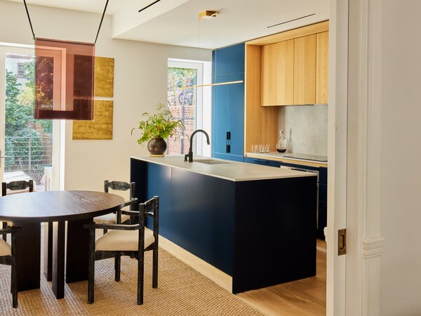 In the dining room, Guillerme et Chambron armchairs from Maison Gerard surround a CB2 table. The ceiling light is by Lambert &amp; Fils. In the kitchen, rich blue cabinetry with wood details from GD Arredamenti is topped with a Caesarstone “Aire Concrete” counter. The gold artwork is by Joyce Billet.