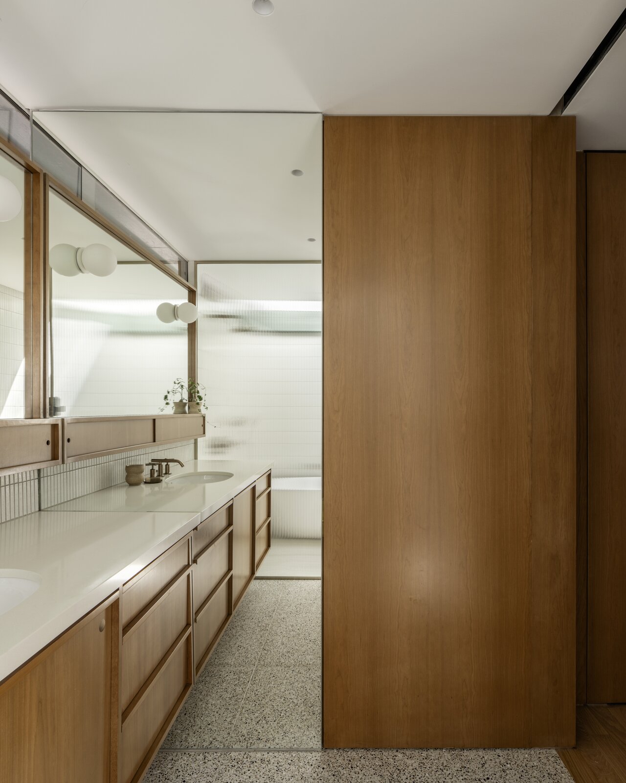 Cover Architecture and EEK Studio designed the custom vanity, which was fabricated by Hardwood Habitat. The wood door conceals the toilet room, while a pocket door separates the bathroom from the bedroom. The terrazzo floor tile is from Cle Tile.