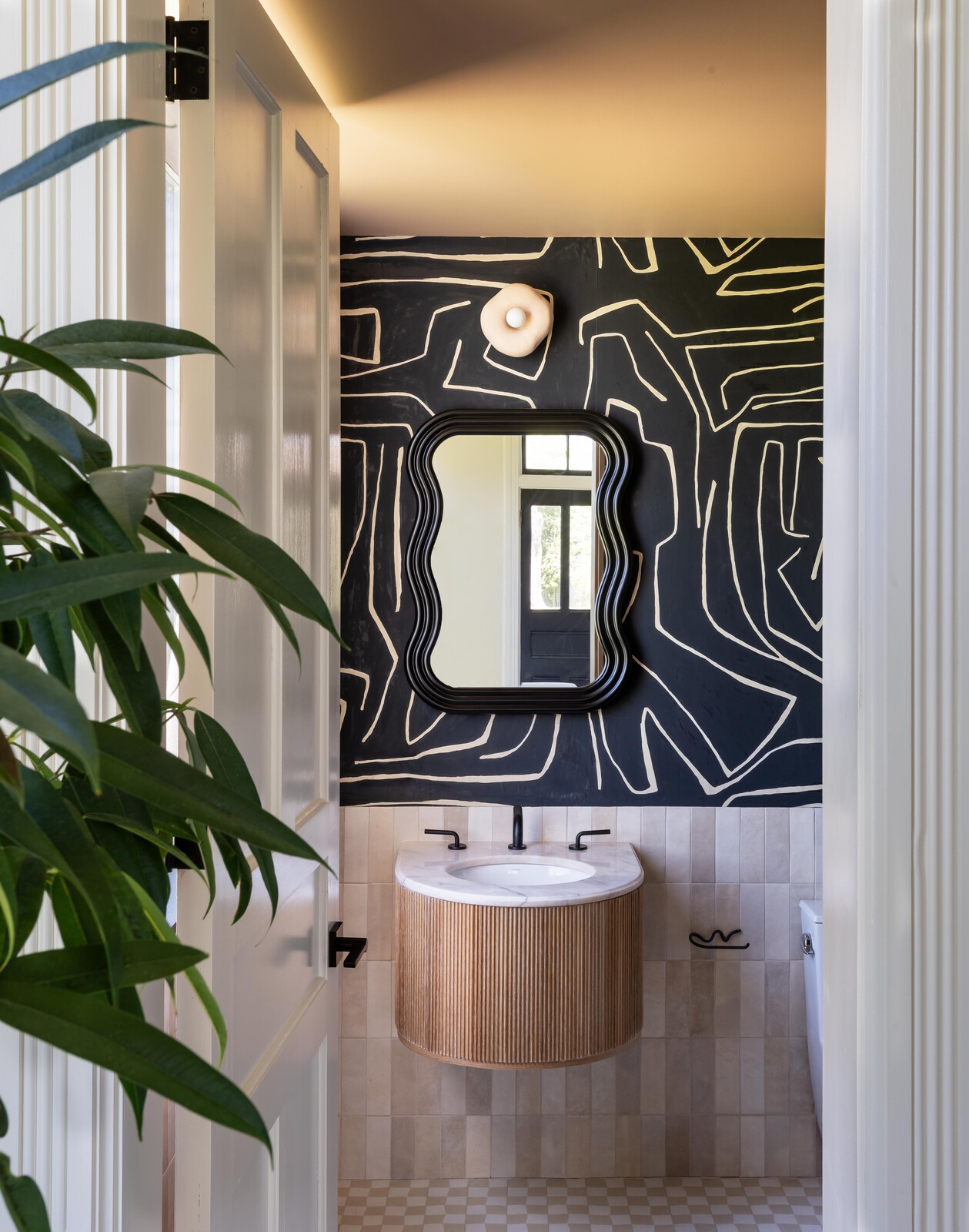Joel designed and built the wall-mounted vanity base to fit the rounded shape of the marble sink surround, which the couple found years ago on their first visit to Hudson. The apron is fashioned from a reeded oak tambour panel. The wallpaper is Kelly Wearstler for Lee Jofa, joined by a Lulu and Georgia mirror and Eny Lee Parker sconce.