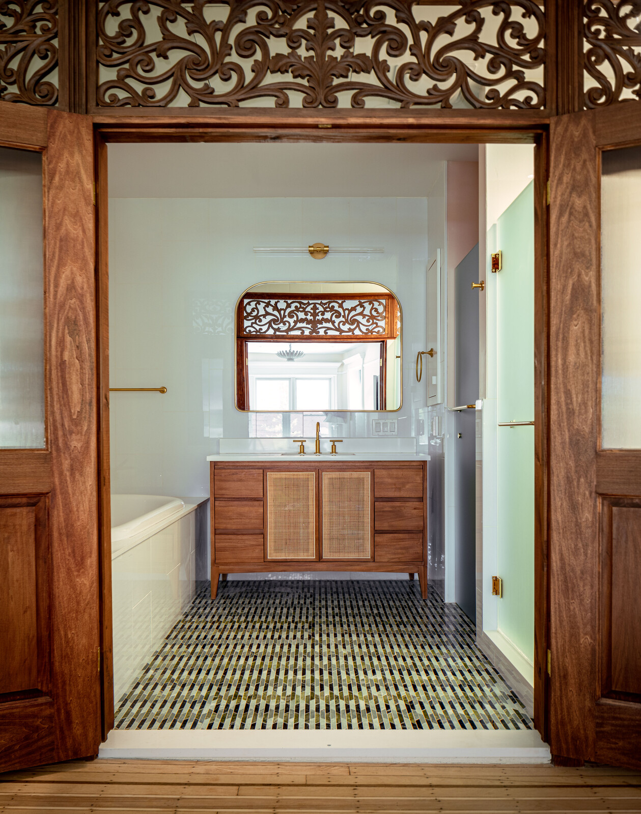 The shower and toilet are tucked in their own enclosures, so the doors can be left open to frame the custom vanity, which was designed to have the same wood tones as the screen but not compete. The flooring is Tappeti Green Blend Mosaic from Artistic Tile.
