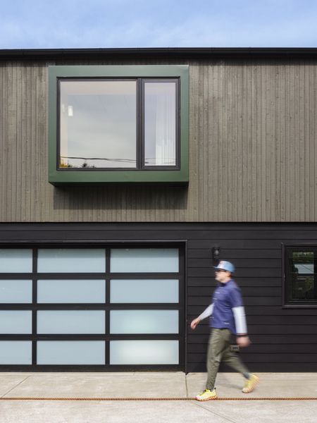 The lower level has an Elegant EL100 aluminum and glass garage door and horizontal siding painted the same color as the main house. The upper level has vertical siding with a bay window differentiated in forest green metal.