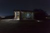 Modern home with Wood Counter, Wood Cabinet, Concrete Floor, Metal Cabinet, Chair, Coffee Tables, Table, Trees, Shrubs, Small Patio, Porch, Deck, Exterior, Metal, Folding Door Type, Metal Counter, Living Space Room Type, Bed, Accent Lighting, Garden, Desert, and Hardscapes. Night view Photo 14 of The Olive Tree House