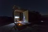 Modern home with Wood Cabinet, Wood Counter, Metal Cabinet, Concrete Floor, Chair, Coffee Tables, Table, Trees, Shrubs, Small Patio, Porch, Deck, Exterior, Metal, Folding Door Type, Metal Counter, Living Space Room Type, Bed, Accent Lighting, Garden, Desert, and Hardscapes. Night view Photo 15 of The Olive Tree House