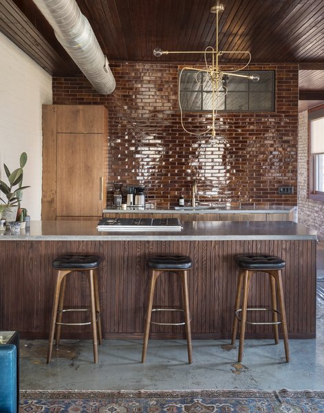 In the kitchenette area, seamless walnut cabinets, poured concrete countertops, and glazed brick tiles introduce minimalistic modern elements.