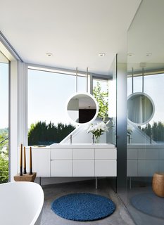 In the master bath, a geometric mirror hangs from the ceiling above, providing continuous views to the hills and sky beyond.