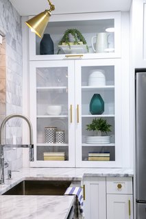 White shaker cabinets, some with glass inserts, combined with brass knobs and pulls, are a modern uptake on a simple style.