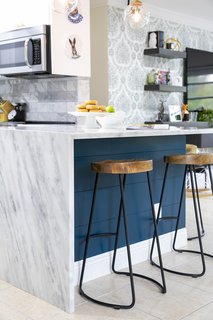 A continuous waterfall edge of the marble countertops creates an impactful statement at the peninsula. Iron and wood bar stools are an industrial accent in the chic space.