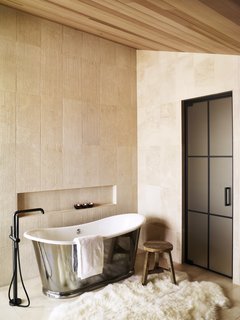 This private bath is a dream retreat after a long day exploring. A tin soaker-tub, lush fur rug, and large tiles in natural tones create an idyllic, calming escape. 