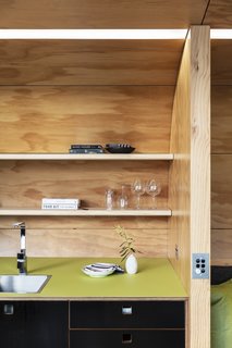 A green linoleum countertop and black cabinets add a pop of color to the wood interiors. Open shelving provides additional storage.