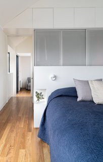 Perforated metal screens connect design elements in the upstairs to the main floor below. A built-in headboard provides clothes storage on one side, and nightstands on the other. 