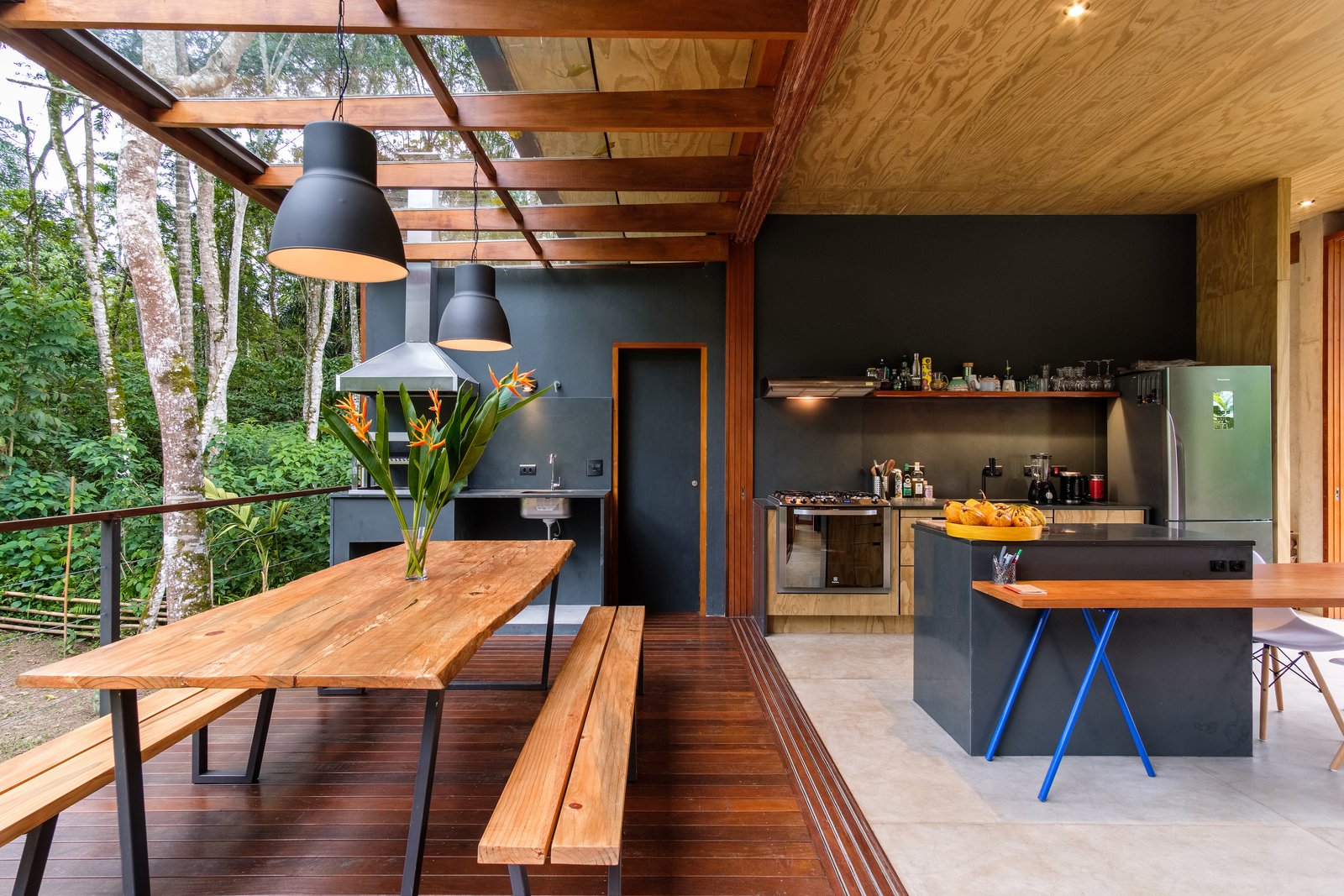 pittaarquitetura Comedor, banco, piso de concreto, mesa, colgante y piso de madera de tamaño medio Un toldo de madera y vidrio brinda protección sin disminuir las vistas.