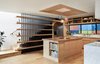 Modern home with Kitchen, Wood Cabinet, Marble Counter, Refrigerator, Dishwasher, Wood Counter, Pendant Lighting, Undermount Sink, Range, Recessed Lighting, Ceramic Tile Backsplashe, Range Hood, and Light Hardwood Floor. Looking Southwest at the kitchen and stair. Beyond, the exterior side yard fence of cement fiber board playfully painted begs for attention, a strong contrast to the neutral palette of wood and soft light inside. The flared ceiling opening of white oak reveals a cluster of pendants from Heather Levine as they fall from the two-story light well centered over the white oak island. The stair is built of cold rolled steel and white oak shelves which filters the light from above. Photo 4 of Ashland Residence