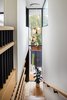 Modern home with Staircase, Wood Tread, Metal Railing, and Wood Railing. From the top of the stair, we gaze beyond the stair landing below to trees and side yard fence enclosure. A half-circle welcome mat of jute outlines the backyard access door (see dutch door in previous images of kitchen and dining). The stair is built of white oak with a cold rolled steel and white oak shelf guardrail and top rail. Tom Dixon brass globe pendants provide "fish-eye" reflections of the staircase. Photo 12 of Ashland Residence
