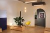 Modern home with Living Room, Bench, Storage, Chair, Ceiling Lighting, Plywood Floor, and Wall Lighting. Rear end of main multi-mode room with door to bathroom and arch to kitchen beyond Photo 12 of Facade/Fasad