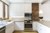 Modern home with Kitchen, Engineered Quartz Counter, White Cabinet, Ceramic Tile Backsplashe, Pendant Lighting, Light Hardwood Floor, Accent Lighting, Ceiling Lighting, Microwave, Range, and Dishwasher. Another view of the kitchen. Photo 7 of Sunset Park Row House