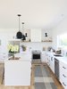 Modern home with Kitchen, Engineered Quartz Counter, White Cabinet, Subway Tile Backsplashe, Light Hardwood Floor, Pendant Lighting, Refrigerator, Wall Lighting, Recessed Lighting, Range Hood, Range, Dishwasher, and Undermount Sink. The entire first floor is centered around the kitchen which features Ikea cabinet bases with Semihandmade fronts painted "White" by Dunn Edwards. The lights by Rejuvenation and Kitchen Aid appliances make this the perfect space for entertaining. Photo 3 of The Simply Simple Home
