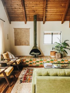 The vintage olive fireplace from The Retro Burn was the first piece Thomas got for the living room. That locked in the color palette of avocado, sorbet pink, and marigold. The Fireclay Tile platform came in when, despite ordering the tallest fireplace she could find, it missed the ceiling by a few feet. The rest of the room is filled with furniture from Joybird. Thomas held fabric swatches up to the fireplace until she found the perfect hue: Key Largo Green. The Soto chairs are swathed in Bentley Daisy with a West Elm Tripod side table between them. Linen curtains in Ecru by Shade Store add drama and height to the space.