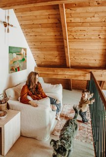 Thomas transformed a loft area just outside the master bedroom into a cozy reading nook with a Shabby Chic sofa, a vintage rug, and side tables. Another painting by Sabina Yannone echoes some of the hues found in the living room tile. The Tara light from Mitzi was just what she was looking for—it's simple, but it counters the extreme angles of the ceiling.