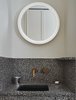 Modern home with Bath Room, Wall Lighting, Stone Counter, Accent Lighting, Undermount Sink, and Glass Tile Wall. The intricate, speckled design of the vanity is paired with clean white walls and an illuminated circular mirror. Photo 7 of Sister City