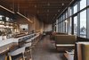 Modern home with Dining Room, Ceiling Lighting, Chair, Bench, Concrete Floor, Stools, Table, Bar, Wall Lighting, Track Lighting, Terrazzo Floor, and Pendant Lighting. While the design in the bar remains clean, the tones are moodier with an added touch of glam. Photo 9 of Sister City