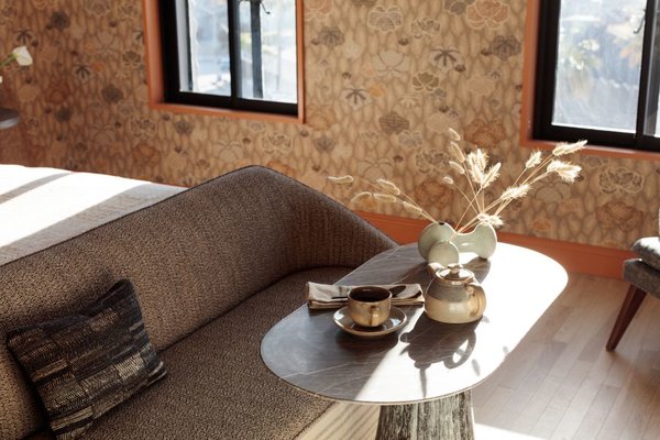 A structured bench at the foot of the bed is balanced with a rounded table and organically-shaped vase.