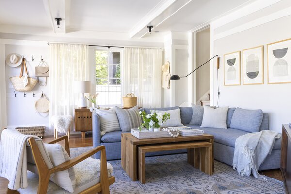 The living area consists of plenty of layering with Saffron and Poe nesting teak tables and coffee table basket tray. A West elm sofa and a Jens Rise Lounge Chair from Design Within Reach serves as anchors over a Saffron and Poe hand-knotted wool rug. Accents include Schoolhouse surface mount lights, a CB2 swivel wall lamp, and midcentury art prints from Printable Studio.