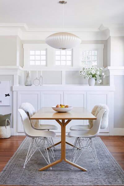 The dining area stands as a clean palette ready for everything from dinner with the family to hosting a gathering over a Houzz Dining table and Eames chairs from Design Within Reach. Overhead a Nelson Saucer Pendant Light illuminates the space, while a vintage rug from Etsy adds a cozy touch.  