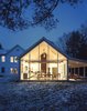 The Floating Farmhouse’s semitransparent addition has a roofline that matches the pitch of the original 1820s farmhouse. A porch, tucked under the side eaves, is cantilevered over a stream that runs through the property. Ikea loungers are illuminated from the interior by commercial gymnasium lights repurposed as pendant lamps. Photo 6 of The Floating Farmhouse modern home