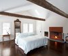 Modern home with Bedroom, Dark Hardwood Floor, Table Lighting, Bed, and Night Stands. A gas fireplace fronted in weathered steel warms up the lofty master bedroom, whose spare decor is framed with beams discovered in a Pennsylvania barn. The Tizio desk lamp is by Artemide. Photo 7 of The Floating Farmhouse